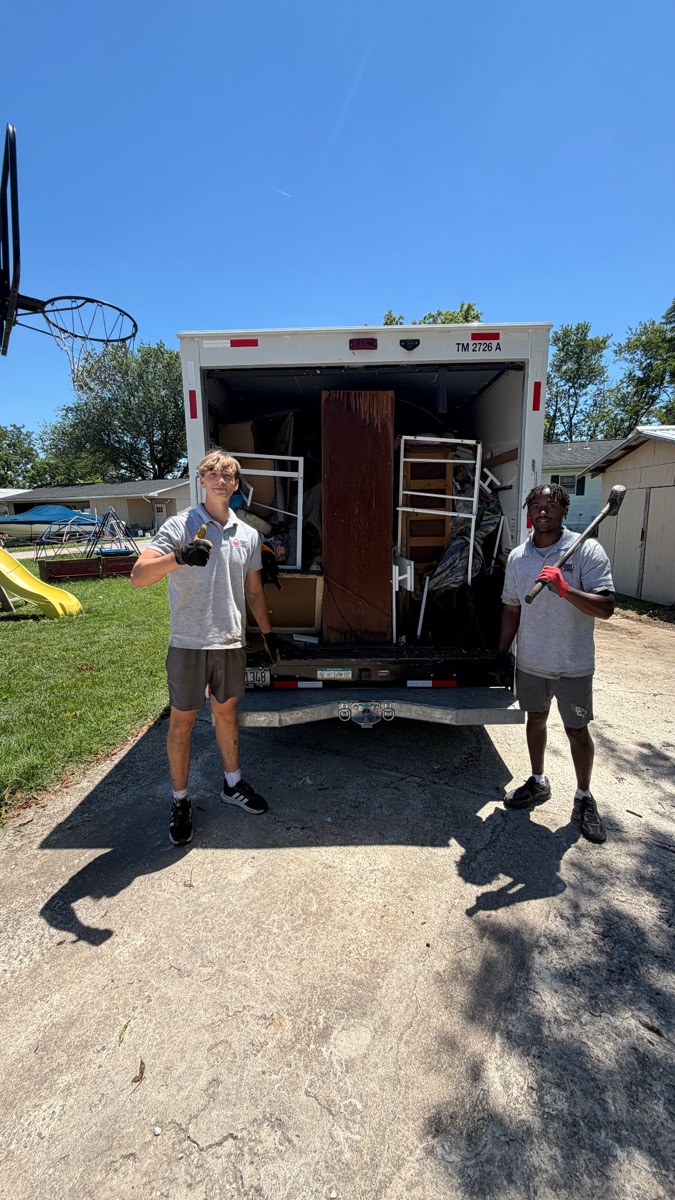 Two 410 Odd Jobs team members in front of a box truck packed with furniture