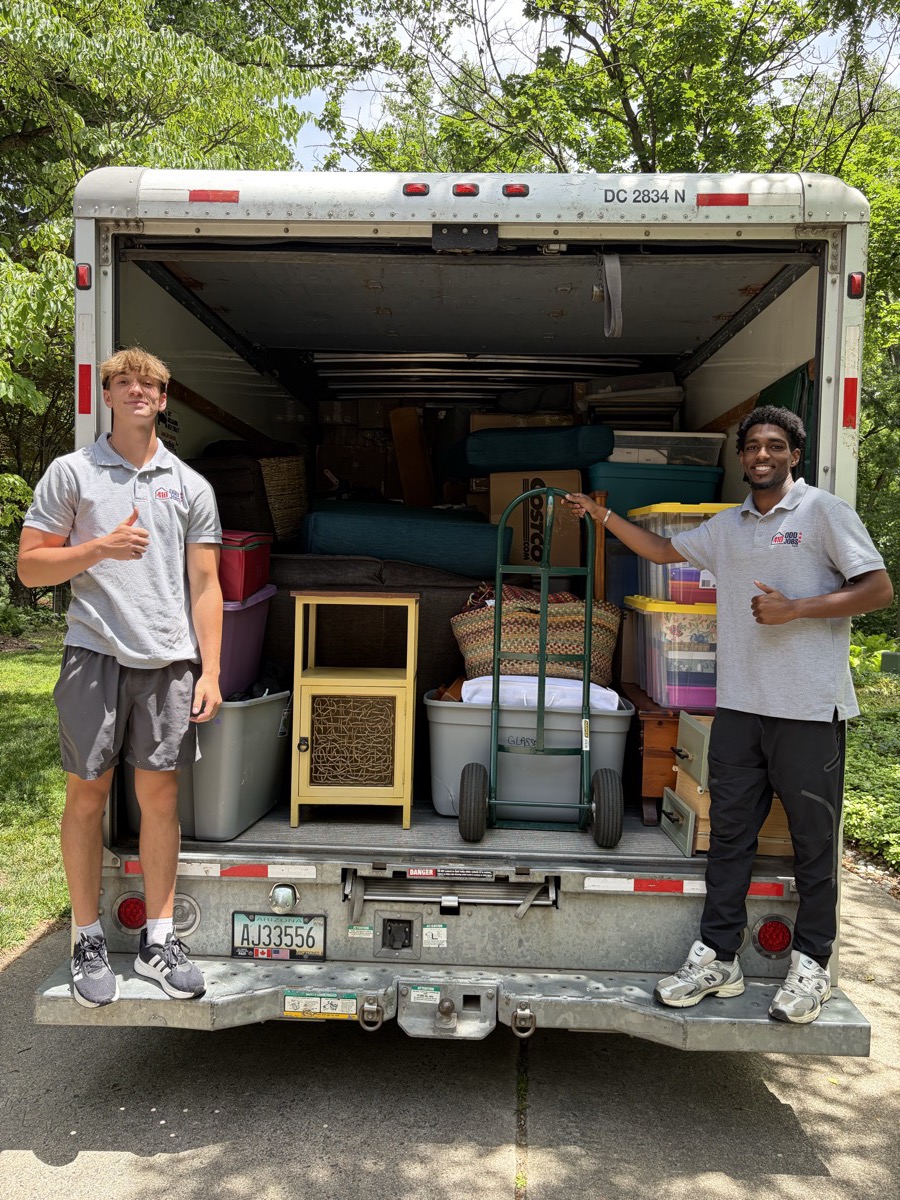 Two 410 Odd Jobs team members on the liftgate of a box truck packed with bins and furniture