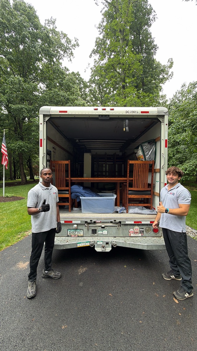 Two 410 Odd Jobs team members with a moving truck loaded with wooden chairs
